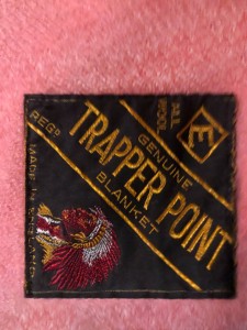 detail showing the original brand label stitched into the corner of the blanket, circa 1948. The label authenticates the “genuine” Trapper Point blanket by marketing the blanket with a racist stereotype of the “Indian Chief”. The label also indicates that in spite of a market in the colonies, the blanket is “Made in England”. Collection of Marlene Kadar.